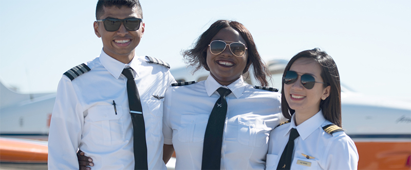 three aviation students smiling in front of plane