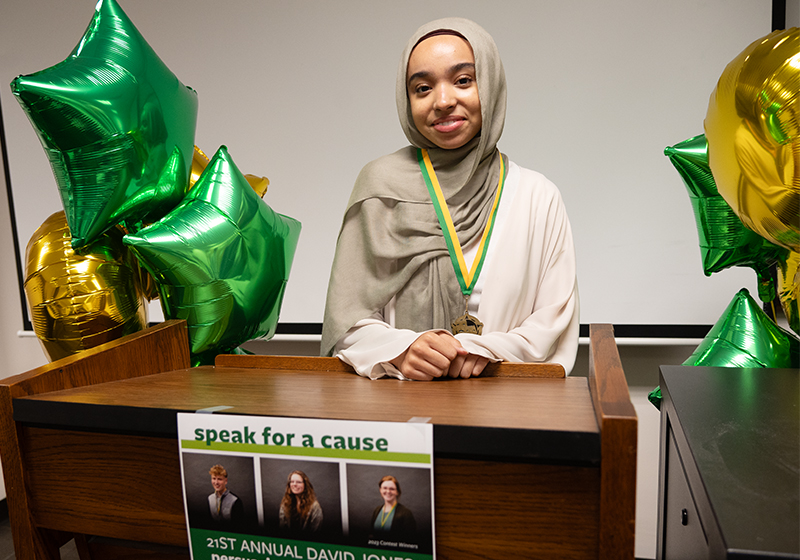 Student wearing a medal at a podium after winning the annual speech contest.